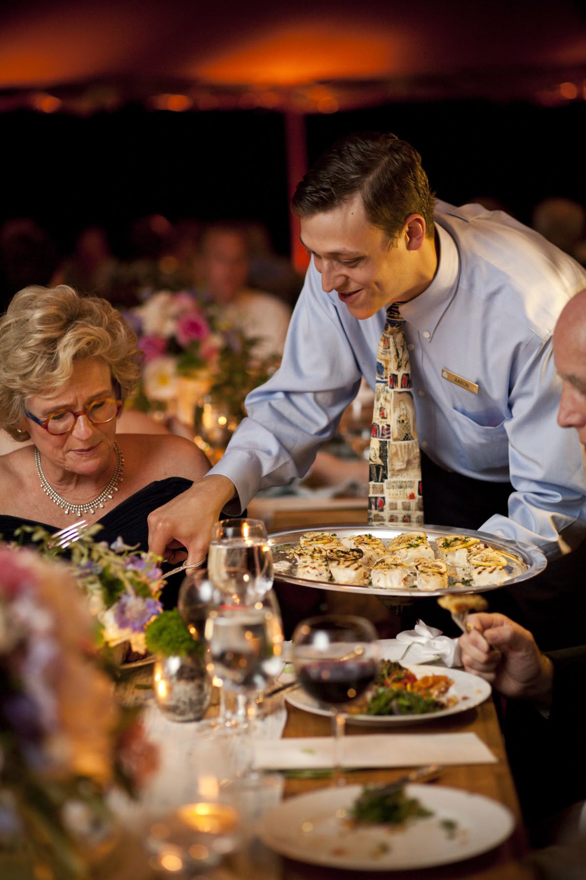 Serveur présentant un plateau à des convives lors d'un dîner de réception aux chandelles